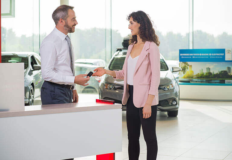 Kvinna som får bilnycklar av Toyota säljare