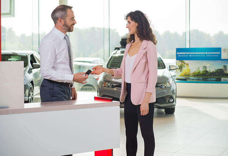 Kvinna som får bilnycklar av Toyota säljare