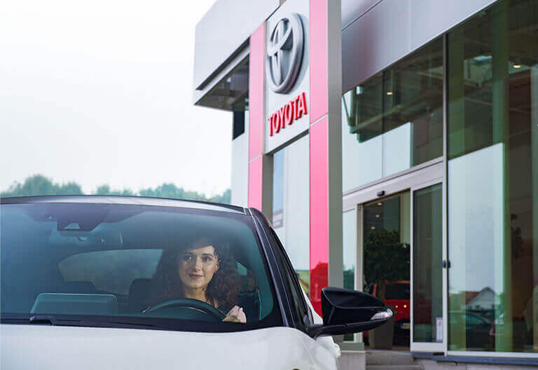 Kvinna som kör en Toyota bil förbi en Toyota anläggning