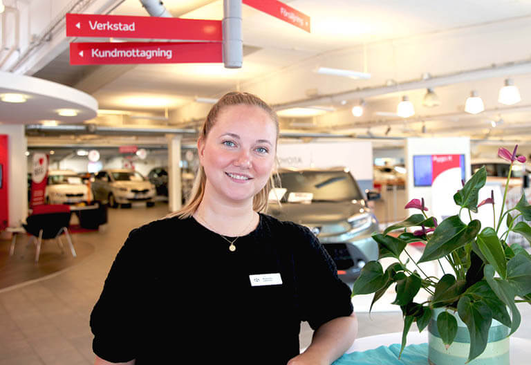En säljare från Lindströms Bil står i bilhallen och tittar in i kameran.