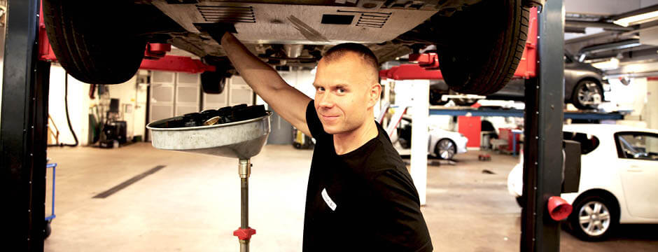 En servicetekniker från Lindströms Bil mekar med en bil och tittar in i kameran.