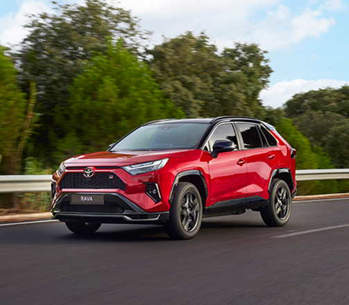 En röd Toyota RAV4 kör i lantlig miljö.